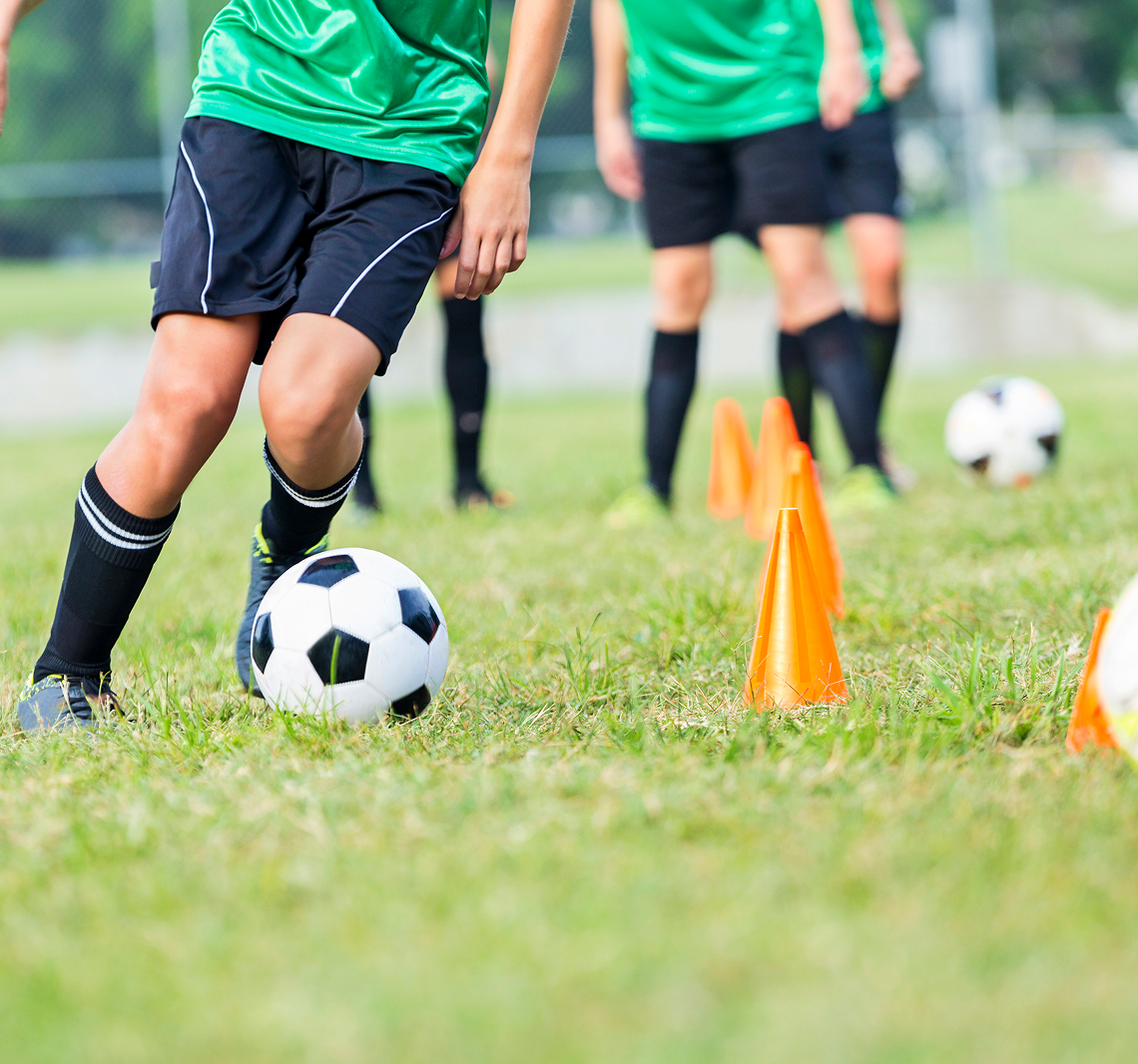 Soccer players practicing with cones on field.